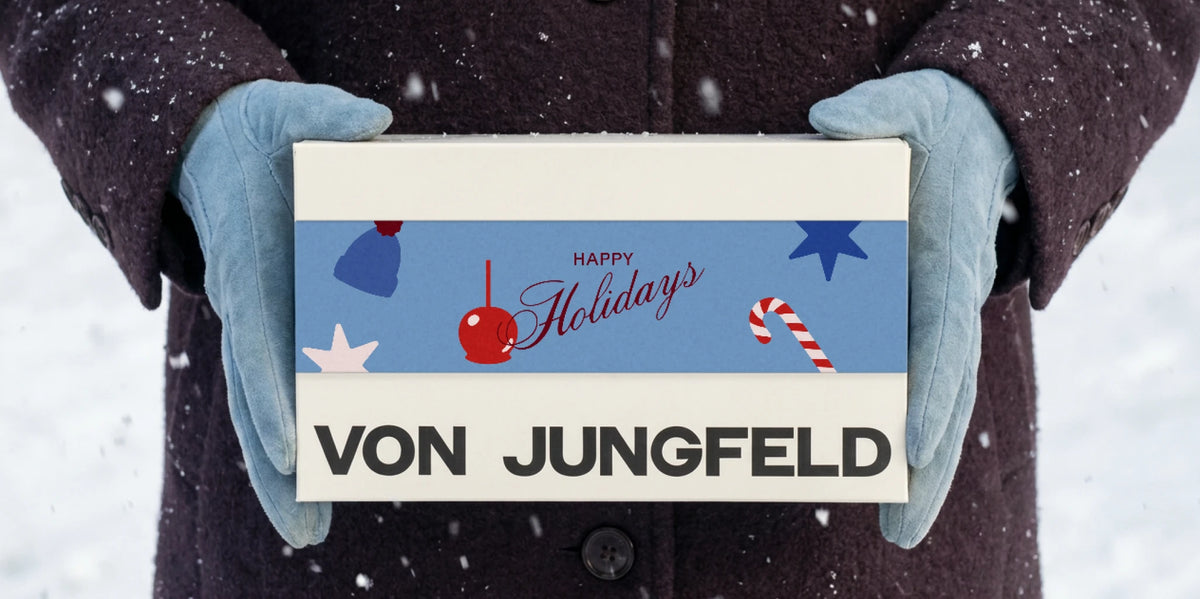 Hände in Handschuhen halten eine Geschenkbox von VON JUNGFELD im Schnee